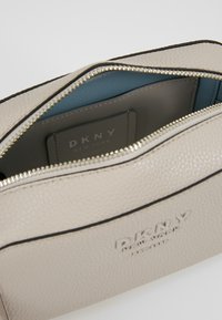 Borsa in pelle beige testurizzata con chiusura a zip, dotata di interno blu e logo DKNY impresso sul davanti. Dettaglio di rifinitura nera visibile.