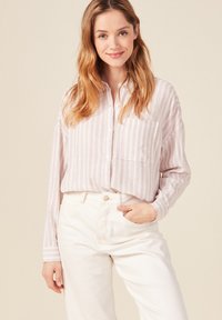 Camicia a righe rosa chiaro con bottoni, taschino frontale, maniche lunghe e vestibilità rilassata, abbinata a pantaloni bianchi a vita alta.