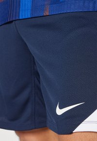 Mørkeblå atletiske shorts lavet af tekstureret stof, med et hvidt Nike-logo nederst til højre og kontrasterende hvide detaljer.