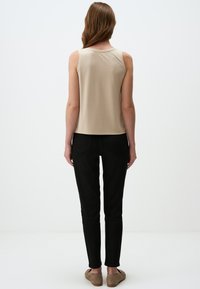 Top beige senza maniche con scollatura arrotondata, abbinato a jeans neri aderenti e calzature nei toni neutri, visto da dietro.