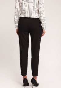 Czarne, dopasowane spodnie o zwężanym kroju, w połączeniu z białą bluzką w wzory oraz czarnymi szpilkami. Gładki materiał, elegancki design.
