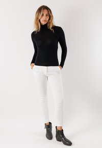 Maglione nero a collo alto, maniche lunghe, design aderente, abbinato a pantaloni bianchi a gamba stretta e stivali neri alla caviglia con cerniere. Look semplice ed elegante.