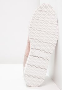 Bílá gumová podrážka se vzorem cik-cak na světle růžovém tenisku, na podešvi je velikost boty 37.