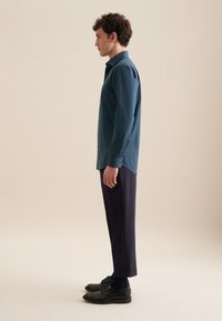 Teal overhemd met knoopjes, een enkele borstzak, lange mouwen en knopen bij de manchetten, gecombineerd met marineblauwe cropped broek en zwarte schoenen.