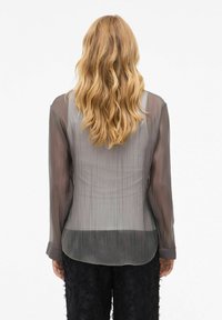 Transparante, langmouwige blouse in grijstinten met een iets donkerder zoom. Kenmerkt zich door een subtiele verticale textuur en een afgeronde achterzoom.