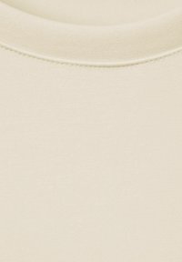 Béžový textil s krátkými rukávy, hladkou a měkkou texturou a kulatým výstřihem. Má jemné švy podél výstřihu.