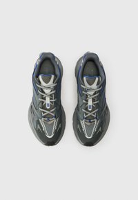 Pelēkas un zilas sporta kedas ar šņorēm, skatītas no augšas uz vienkārša balta fona.