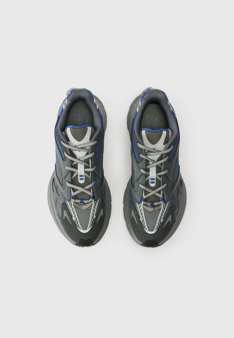 Et par grå og blå atletiske sneakers med snørebånd, set ovenfra på en ensfarvet hvid baggrund.