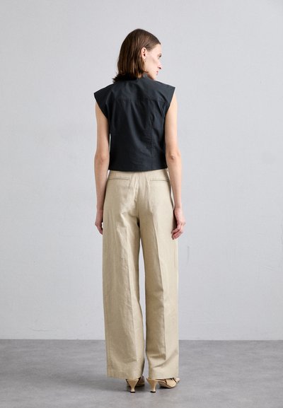 Top negru scurt, fără mâneci, cu umeri structurați, asociat cu pantaloni bej cu croi larg și pantofi cu toc deschiși la culoare.