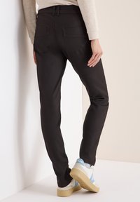 Svart slim-fit byxor med en mjuk textur, med två bakfickor och en midjehög linning, i kombination med ljusa sneakers.