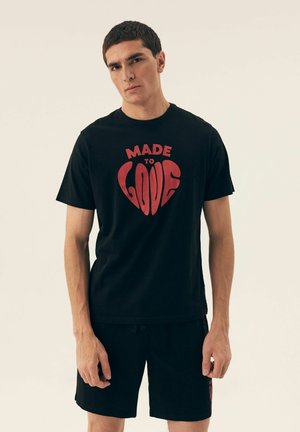 Black cotton t-shirt featuring a red heart graphic with the text "MADE TO LOVE" in a bold font. Short sleeves and a relaxed fit.