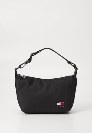 Sac à main en tissu noir avec une fermeture éclair sur le dessus et une bandoulière courte et ajustable. Présente une écusson logo avec des accents rouge, blanc et bleu. Texture lisse.