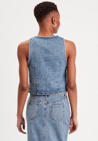 Haut court en denim bleu clair sans manches avec une finition délavée. Il présente des surpiqûres, un col rond et une silhouette ajustée.