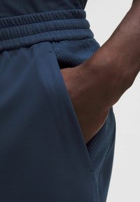 Granatowe szorty sportowe wykonane z lekkiego materiału o teksturowanym wykończeniu, wyposażone w siateczkową kieszeń i elastyczny pas dla komfortu.