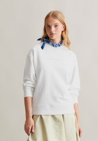 Witte sweatshirt met geribbelde manchetten en onderrand, voorzien van een klein blauw logo op de borst. Gestyled met een blauwe, gemusterde sjaal om de nek.