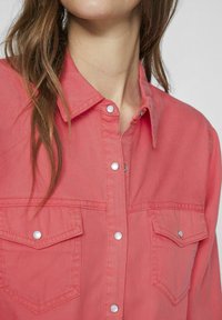 Camicia button-up color corallo con colletto, due tasche sul petto con flap e chiusura a scatto, e un tessuto testurizzato.