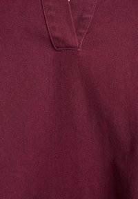 Detailný záber na bordovú látku s diagonálnou textúrou tkania a zošitým V-štehom v strede.