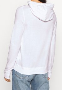 Vit huvtröja med långa ärmar, mjukt tyg, ribbade mudd och nederkant, taggad på baksidan, tillsammans med ljusblå jeans.