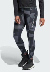 Zwart en grijs gemêleerde leggings met een aansluitend ontwerp. Kenmerken zijn een zijvak en een logo op het onderbeen, gecombineerd met zwarte sneakers.