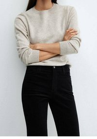 Beige knitted sweater with a round neckline, long sleeves, and ribbed cuffs, paired with high-waisted black jeans, featuring a classic fit.