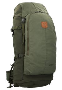 Mochila verde con un tejido duradero, equipada con correas laterales, bolsillos con cremallera y un parche de cuero con el logo. Diseño compacto, con múltiples compartimentos.