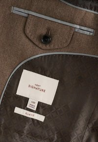 Brown wool-blend suit jacket interior with two labels: "NEXT SIGNATURE" and "SLIM FIT." Features a button and gray satin lining.