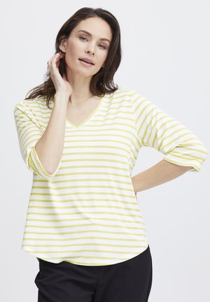 Top a V con righe gialle e bianche, maniche a tre quarti, tessuto morbido, orlo curvo, indossato con pantaloni neri. Design semplice e casual.
