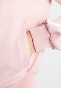 Roze lange mouwen top met een soepele textuur, zijzak en ribbelmanchetten. De stof lijkt lichtgewicht en licht gekreukt.