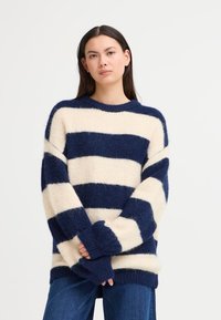 Maglione a righe in blu navy e crema, realizzato in materiale morbido e peloso. Presenta un collo rotondo e maniche a sbuffo.
