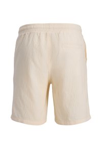 Shorts beige en tissu texturé, taille élastique, et une seule poche arrière. Le design présente une coupe décontractée et des lignes épurées.