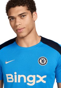 Sininen jalkapallopaita lyhyillä hihoilla, jossa on mustia yksityiskohtia, Chelsea FC:n logo ja "Bingx" valkoisilla kirjaimilla edessä, valmistettu teksturoidusta kankaasta.