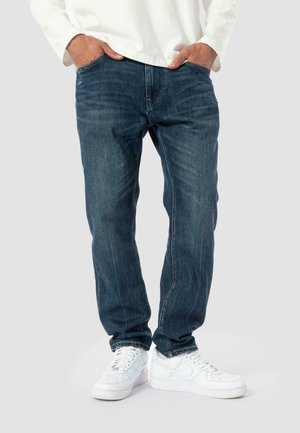 Denim jeans in dark blue with a straight-leg design, featuring visible stitching and slight fading. Paired with white sneakers.