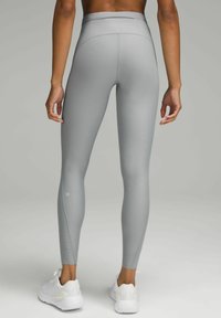Jasnoszare legginsy z wysokim stanem, z teksturowanym wzorem i dopasowanym krojem. Zawierają detal z logo na dolnej części nogawki. Noszone z białymi butami sportowymi.