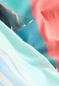 Gros plan sur des plis de tissu texturé montrant des couleurs bleu sarcelle, corail, bleu clair et beige avec un motif floral sur la section bleu sarcelle.