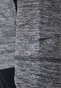 Grauer sportlicher Stoff mit einem strukturierten Melange-Muster, verziert mit einem schwarzen Nike-Logo auf dem Ärmel und sichtbaren Nähten.