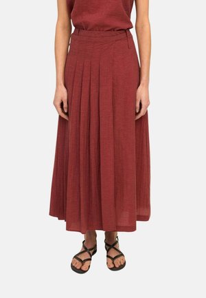Mujer con una falda de talle alto, plisada, hasta el tobillo de color óxido con un top a juego y sandalias negras de tiras.