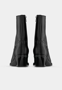 Melnas potītes zābaki, izgatavoti no gludas ādas, ar elegantu dizainu, ar rāvējslēdzēju aizmugurē un masīlu, spīdīgu papēdi.