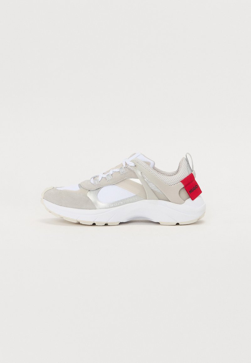 Sneakers mit einem Obermaterial aus hellgrauem Wildleder und Mesh, weißen Akzenten und einer roten Fersenschlaufe. Sie verfügen über ein reflektierendes Detail und eine strukturierte Sohle.
