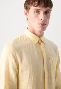 Light yellow linen shirt featuring a button-down collar, front pocket, and a textured fabric for a casual look.