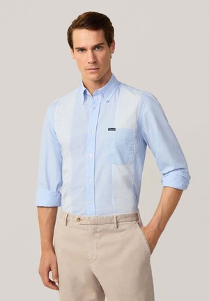 Lichtblauw button-up shirt met horizontaal gestreepte panelen en een borstzak; effen mouwen zijn opgerold. Draag het met beigerkleurige broeken.