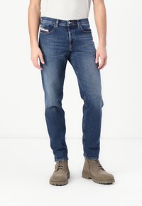 Jeans in denim blu scuro con vestibilità slim, design a cinque tasche e leggera scoloritura; abbinati a stivali alla caviglia color tortora con superficie testurizzata.
