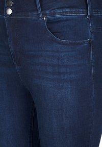 Temno modri kavbojki iz denima z gladko teksturo, opremljeni z dvema kovinskima gumboma, sprednjim žepom in slim fit zasnovo.