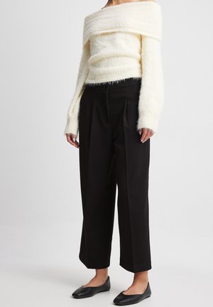 Krémový, off-the-shoulder, huňatý sveter skombinovaný s čiernymi širokými nohavicami s vysokým pásom a čiernymi plochými topánkami. Sveter má dlhé rukávy a textúrovaný vzhľad.