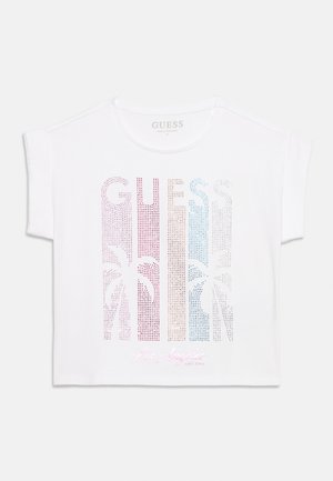 Camiseta corta blanca de manga corta con "GUESS" en piedras de colores y diseños de palmeras, con "Los Angeles" impreso en cursiva debajo.