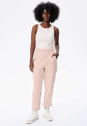 Roze broek in blushkleur met een taps toelopende pasvorm en elastische tailleband. Gecombineerd met een witte geribde tanktop en witte hoge sneakers.
