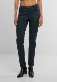 Jeans ajustados de color azul marino hechos de una tela suave, con una cintura de altura media, bolsillos y detalles metálicos en el botón y los bolsillos.