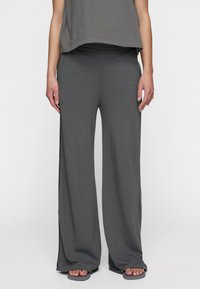 Pantaloni grigi a gamba larga realizzati in tessuto morbido, con vita alta e spacco laterale, abbinati a un top grigio largo a maniche corte.
