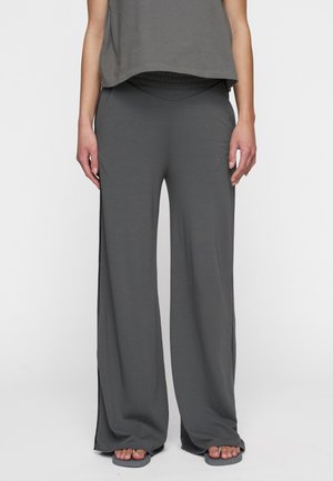 Pantaloni grigi a gamba larga realizzati in tessuto morbido, con vita alta e spacco laterale, abbinati a un top grigio largo a maniche corte.