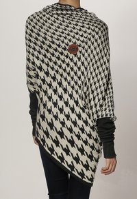 Gehaakte poncho in een beige en zwart houndstooth patroon, met een ronde zoom en brede mouwen. Bruine logo detail nabij de halslijn.