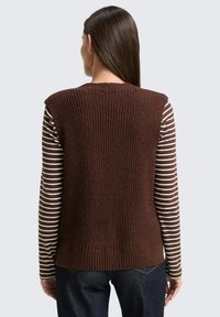 Bruine gebreide vest met een gestructureerd ribpatroon, mouwloos ontwerp. Draag over een gestreept langemouwenshirt, gecombineerd met donkere jeans.